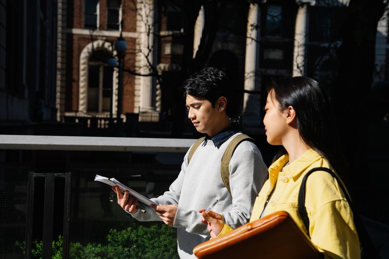 Two students looking through notes on a walk outside