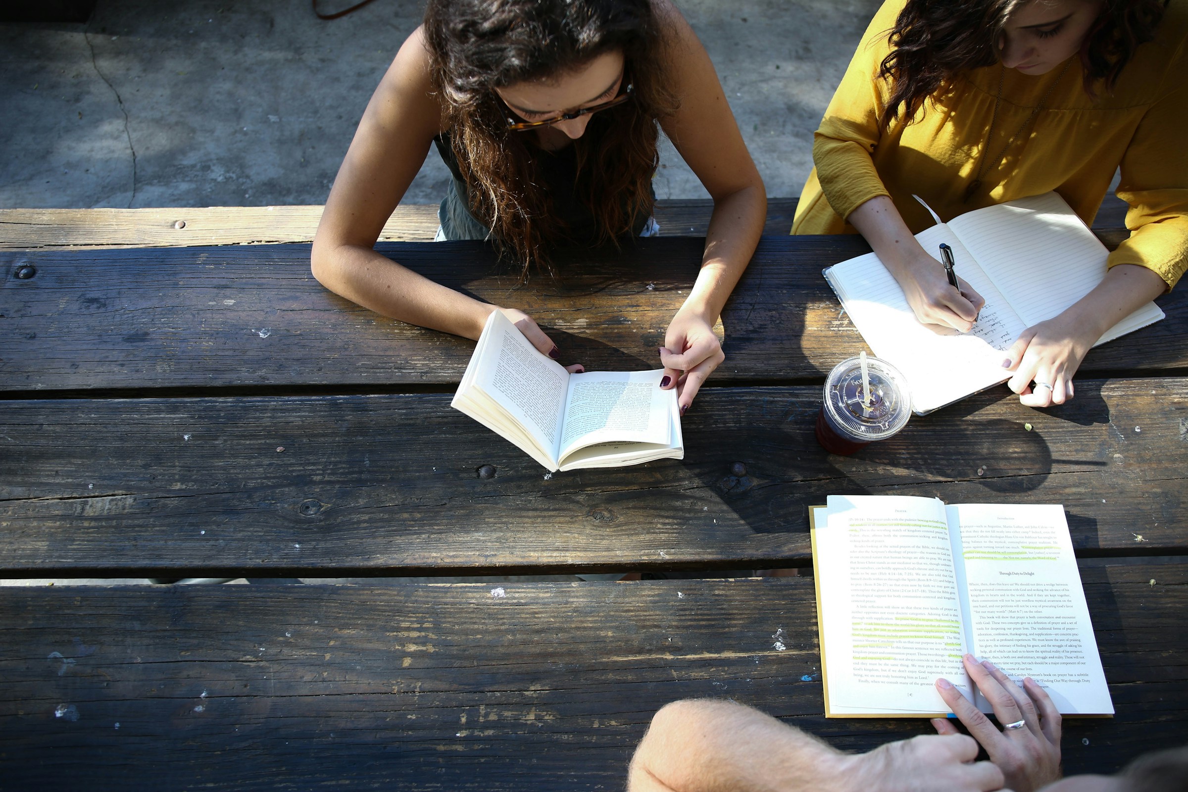 People reading and taking notes together at a wooden table outdoors